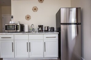 A kitchen with white cabinets, a stainless steel refrigerator, a microwave, a coffee maker, and decorative wall art.