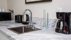 Una cucina moderna con lavello in acciaio inox, bollitore, macchina del caffè e piano di lavoro in marmo.