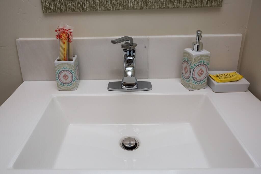 A bathroom sink with a modern faucet, two decorative containers, and a soap dish.