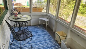 Une véranda avec un tapis bleu à motifs, une table avec des chaises et une vue sur une maison et la verdure environnante.