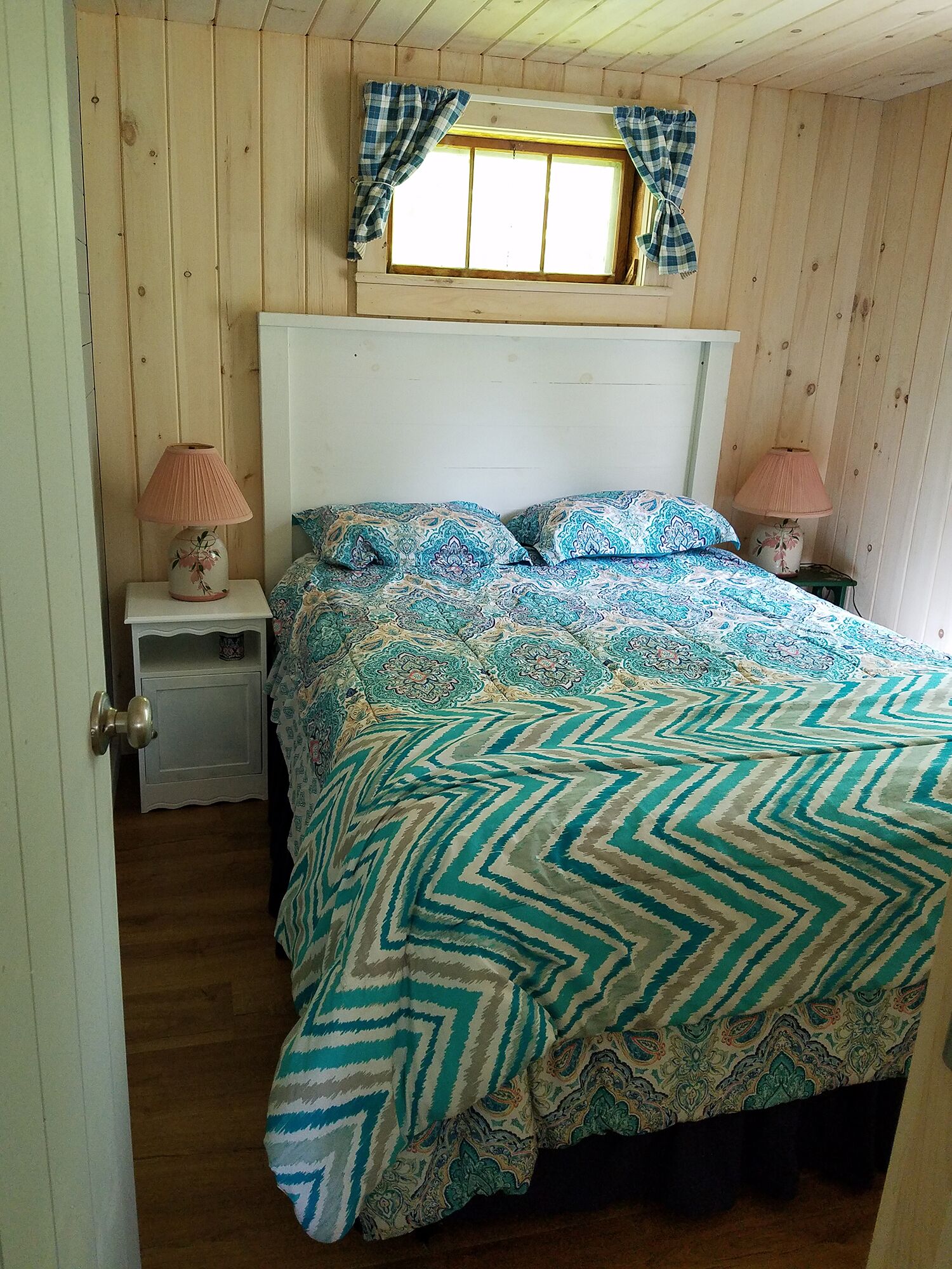 Een slaapkamer met een bed, twee nachtkastjes, een raam met gordijnen en een deur.