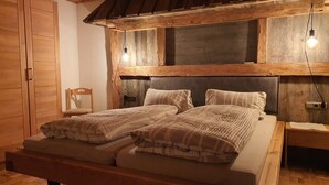 Een houten bed met hoofdeinde, twee nachtkastjes, een stoel en een kledingkast in een landelijke kamer.