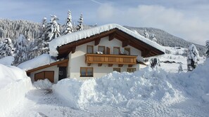 Un chalet doté d’un balcon en bois, entouré d’arbres couverts de neige et avec une chaîne de montagnes en toile de fond.