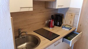 Een kleine keuken met een roestvrijstalen spoelbak, een zwart snijplank, een rode elektrische waterkoker en een koffiezetapparaat.
