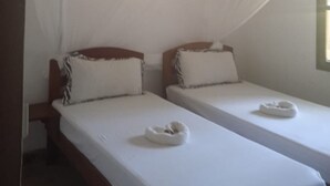 A room with two beds, each with a white mattress and pillow, and a mosquito net draped over the beds. - Johari Villas (Malindi)