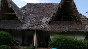 A thatched-roof building with a stone patio, two red lounge chairs, and a small garden area. - Johari Villas (Malindi)