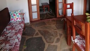 A room with a stone floor, a wooden table with chairs, a sofa with a patterned cushion, and a zebra-patterned rug. - Johari Villas (Malindi)