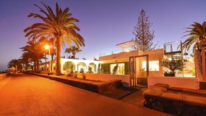 Un hotel moderno con fachada de vidrio, asientos exteriores y palmeras.