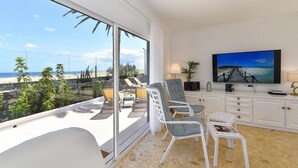 Una sala de estar moderna con un amplio ventanal corredero que da a un balcón con vistas a la playa.
