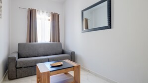 A modern living room with a grey sofa, a wooden coffee table, and a large mirror on the wall. - Modern 1BR Retreat by the Promenade (Gzira)