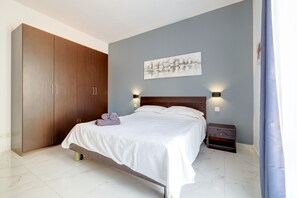 A bedroom with a bed, a nightstand, a wall-mounted lamp, and a large wardrobe. - Modern 1BR Retreat by the Promenade (Gzira)