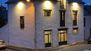 Un edificio de dos pisos con techo inclinado, varias ventanas con persianas y una chimenea visible.