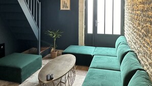 Una sala de estar moderna con una pared azul oscuro, una escalera, un sofá verde, una mesa de centro redonda y una pared con textura de piedra.