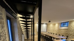 Un salón de conferencias con una larga mesa, paredes de piedra y un diseño moderno en el techo.