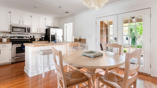 Una cocina moderna con armarios blancos, electrodomésticos de acero inoxidable y una mesa redonda con sillas de mimbre.