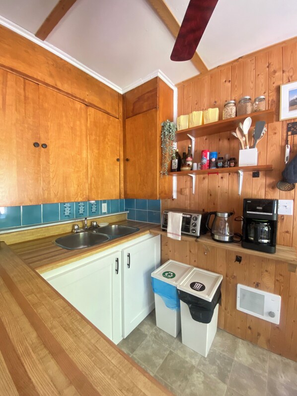 Una cocina con armarios de madera, un lavamanos, un tostador, una cafetera y un cubo de basura.