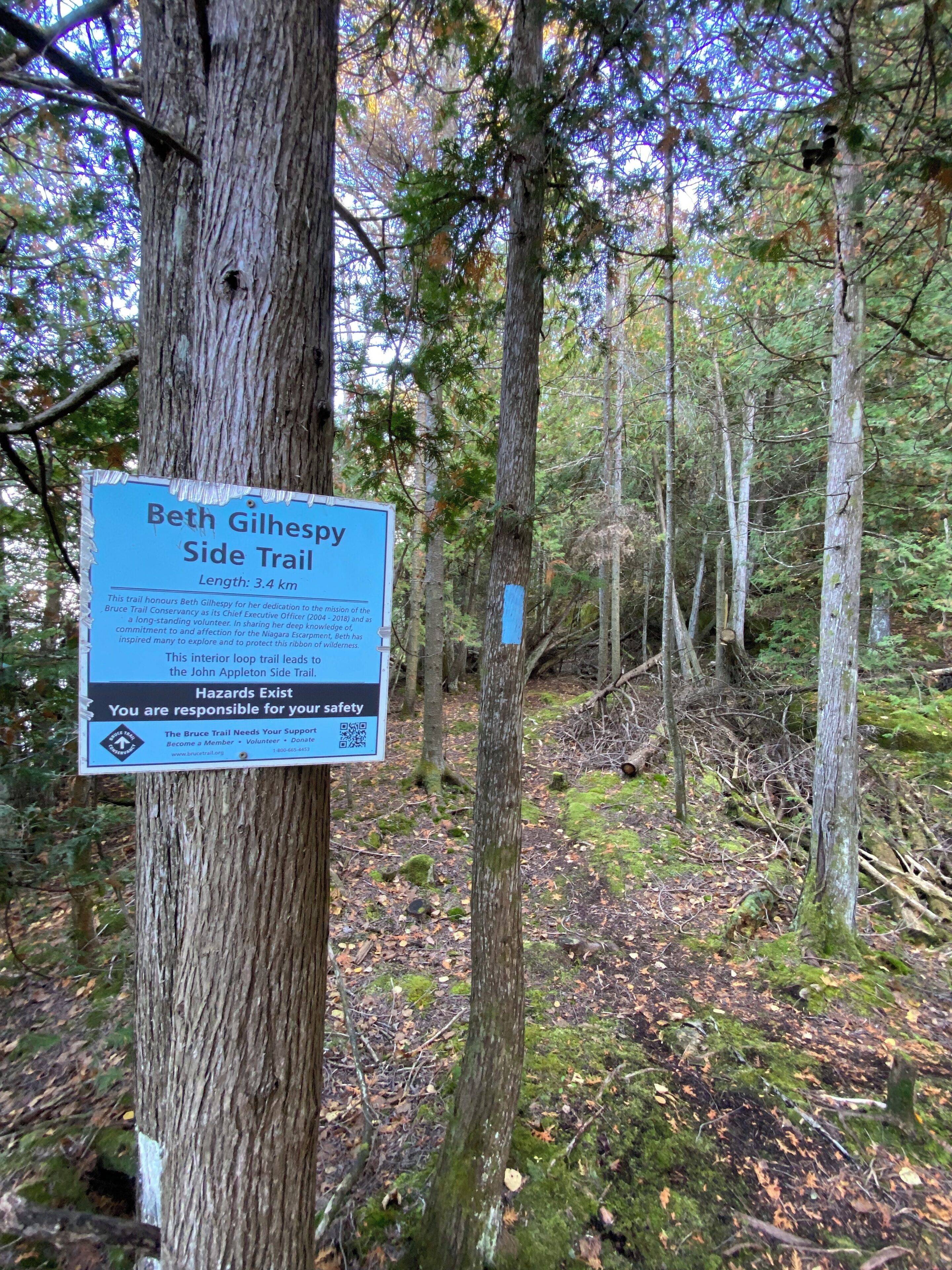 A sign on a tree in a forested area, indicating the Beth Gilhapy Side Trail, with a length of 3.4 km.