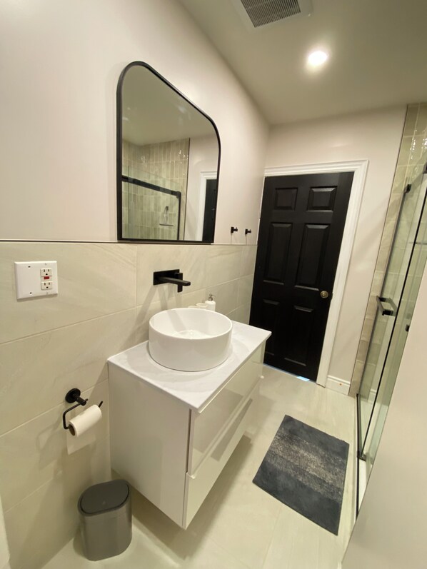 Un baño moderno con un tocador blanco, un espejo grande, una puerta negra y una cabina de ducha de vidrio.
