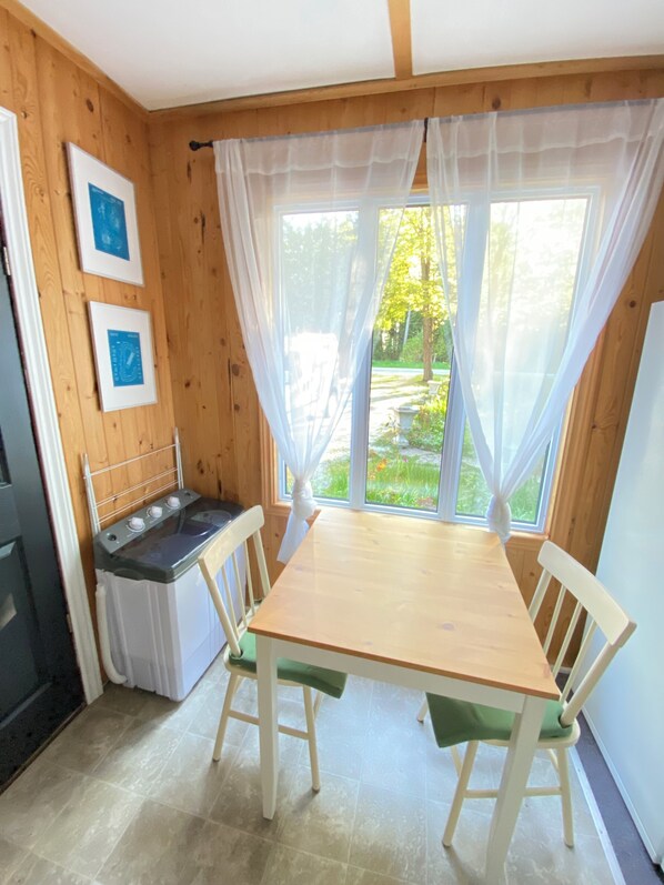 Une petite cuisine avec une table et des chaises en bois, un poêle et une fenêtre ornée de rideaux légers.