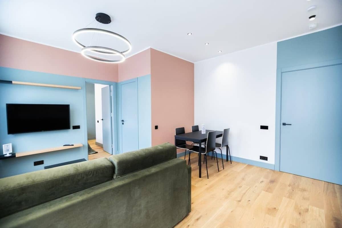 A modern living room with a flat-screen TV, green sofa, and a dining area with a table and chairs.