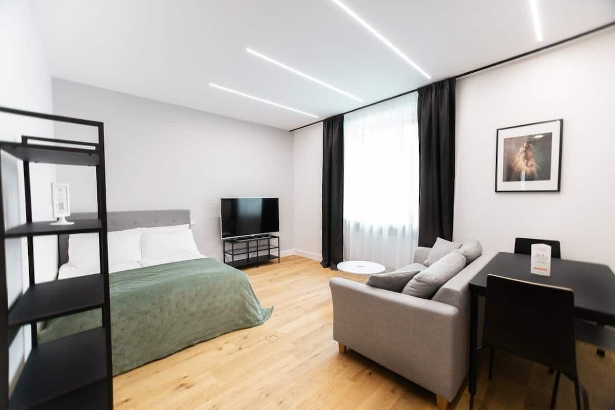 A modern hotel room with a bed, a sofa, a TV, and a desk.