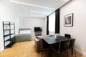 Een moderne hotelkamer met een bed, een televisie, een eettafel met stoelen, een boekenkast en een ingelijst schilderij aan de muur.