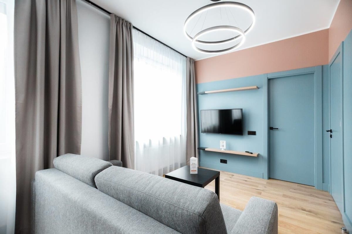 A modern living room with a grey sofa, a small black table, a flat-screen TV mounted on the wall, and a blue door.