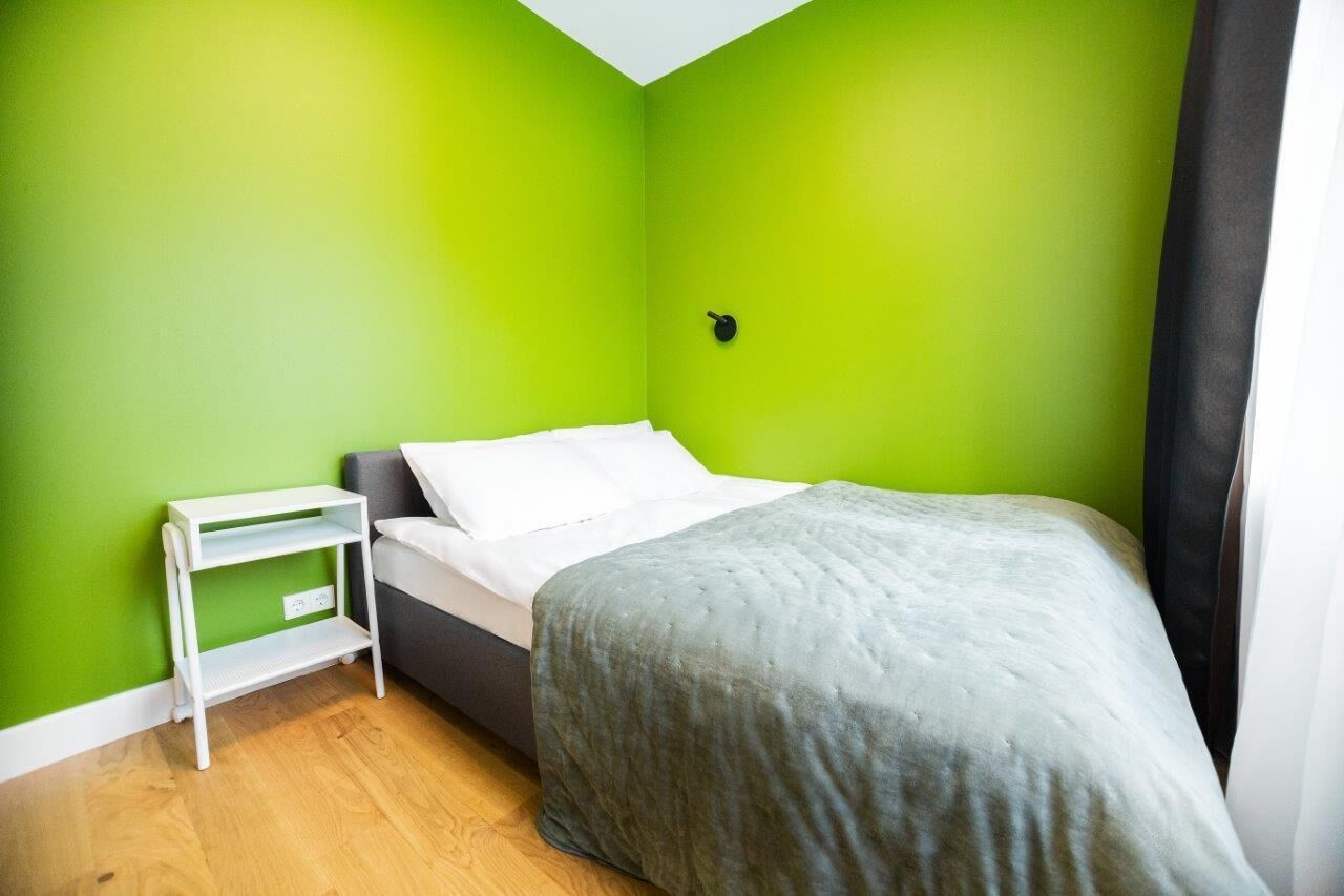 Una stanza con un letto, un comodino bianco e una parete verde.