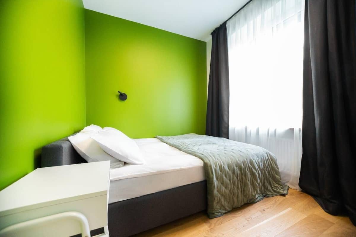 A room with a bed, a desk, and a window with curtains.