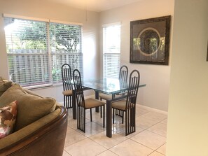 A dining area with a glass table and four chairs, a sofa with a floral pillow, and a framed artwork on the wall. - WEF, 3 Bedroom 3.5 bath wellington home just min to show grounds (Wellington)