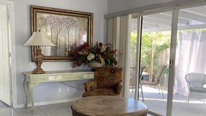 A living room with a sofa, a round coffee table, a side table with a lamp, a framed painting, and a vase with flowers.