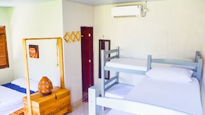 Quarto com beliches, um baú de madeira, ar condicionado fixado na parede e uma porta.