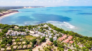 Vista aérea de um resort à beira-mar, com vários edifícios, uma praia e águas azul-claras.