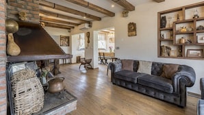 Een gezellige woonkamer met een open haard, houten balken, een leren bank en een rustieke inrichting.
