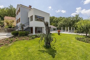 Una casa moderna de dos pisos con un césped bien cuidado, una bicicleta apoyada en un árbol y un cielo despejado.