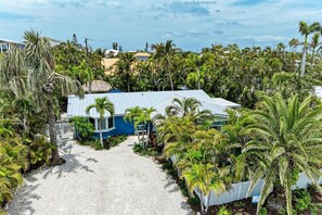 A beachfront property with a thatched-roof structure, surrounded by dense palm trees and a gravel driveway.