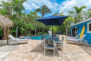 A pool area with lounge chairs, a table, and a blue umbrella.