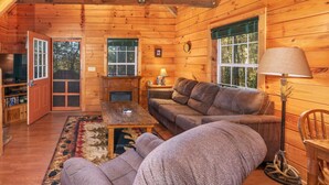 A log cabin interior with a sofa, coffee table, lamp, and a fireplace.
