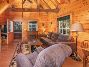 Ein Holzblockhaus-Innenraum mit einer Couch, einem Couchtisch, einer Lampe und einem Kamin.
