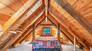 An attic bedroom with a bed, wooden beams, and a window.