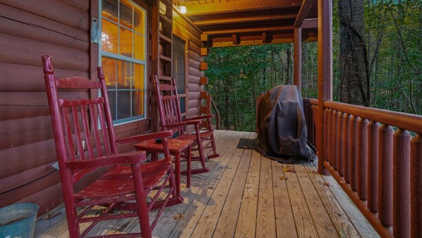 A wooden cabin with a porch, red chairs, a ladder, and a covered area.