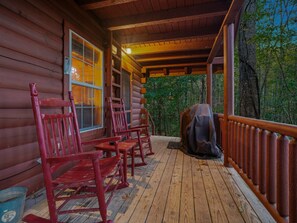 Une cabane en bois avec un porche, des chaises rouges, une échelle et un espace abrité.