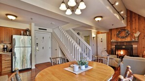 A modern kitchen with a large refrigerator, wooden cabinets, and a dining area with a wooden table and chairs. - The Sky's the Limit at Mountain Green 2BD/2BA: Close to Slopes / Discount Tickets (Killington)