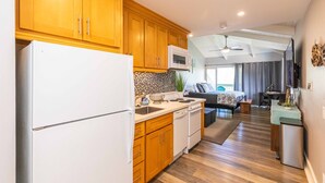 A modern kitchen with wooden cabinets, a white refrigerator, a microwave, and a dishwasher. There is a dining area with a table and chairs, and a living room with a sofa and a TV. - Great rates at Kihei Bay Surf G259 Comfortable Studio Space! (Kihei)