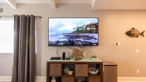A living room with a television displaying a beach scene, a wooden cabinet with storage drawers, a fish decoration, and a curtain. - Great rates at Kihei Bay Surf G259 Comfortable Studio Space! (Kihei)