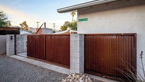 A gated entrance with a metal gate and a concrete wall, a street sign, and a clear sky. - Solar powered, central, private, secure guest house! (Tucson)