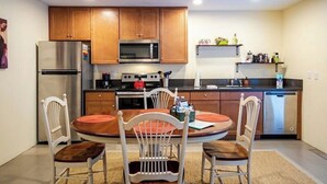 A compact kitchen with wooden cabinets, a stainless steel refrigerator, a microwave, an oven, and a dishwasher. There is a round dining table with four chairs. - Solar powered, central, private, secure guest house! (Tucson)