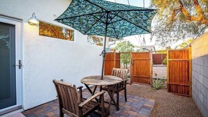 A patio with a table and chairs, a patterned umbrella, and wooden fencing. - Solar powered, central, private, secure guest house! (Tucson)