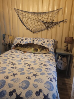 A bed with a blue and white sea-themed bedspread, a net above the bed, and a nightstand with a lamp and a bag.