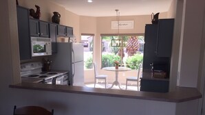 Una cucina compatta con fornello, forno a microonde e frigorifero. C'è un'area pranzo con tavolo e sedie, e una vista su un giardino tramite una porta vetrata.